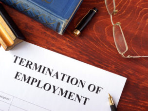 A paper that says "Termination of Employment" and a notebook, pens, and glasses are around the paper