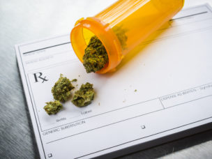 An orange pill tube with medical marijuana spilling out of it on top of a prescription pad.