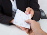 Closeup of a businessman passing another man a check.
