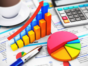 Macro view of a calculator, bar graph charts, pie graph and ballpoint pen on financial reports with colorful data and selective focus effect.