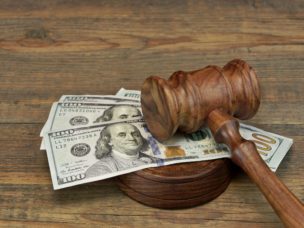 A gavel laying on four 100 dollar bills on a wooden surface.