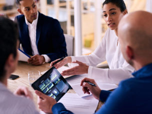 business meeting between four upper management board members in the new modern office conference room with technology integrated in the form of a tablet.