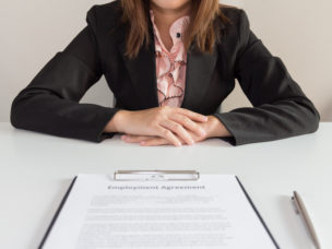 A business woman sitting across a table with a paper titled "Employment Agreement."