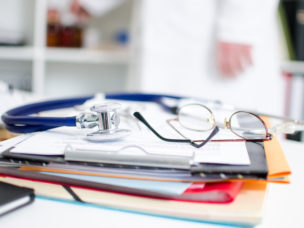 Files, stethoscope and glasses on a doctor's desk.