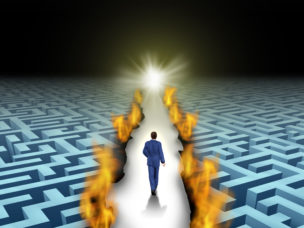 man walking towards light trailblazing path through maze with flames on each side