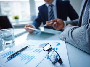 Image of financial documents at workplace and businessmen discussing ideas near by with a close up on the graphs they are to discuss.