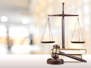 A wooden gavel, a justice scale, and books in focus with a blurry background.