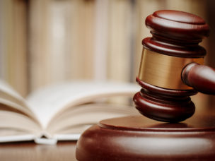 Wooden gavel resting on its end on a wooden table in front of an open law book conceptual of a judge or courtroom.