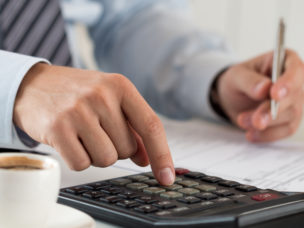 Close up of a male using a calculator to write down important information on paper.