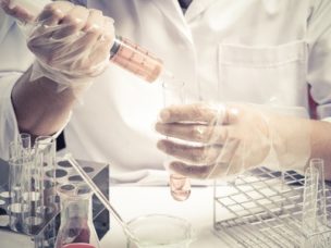 Conical flask in scientist's gloved hand with lab glassware background. Laboratory research concept.