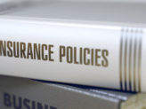 Stack of books with a book titled "Insurance Policies." Book title on spine. Closeup view.