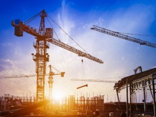 Construction site with multiple cranes and sunset of blue and white as the background.