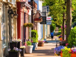 Colorful row of quaint shops and businesses with woman walking dog on the sidewalk.