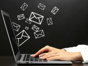 laptop with hands typing and black wall with white envelopes on it