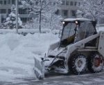a snow plow plowing up snow and trees covered with snow in the background