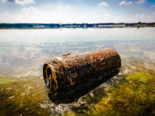 rusted garbage can contaminating a body of water