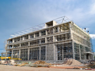 a building in the middle of construction with work machines out front and blue sky in the background