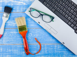 laptop with glasses and two paint brushes on a blue wooden surface