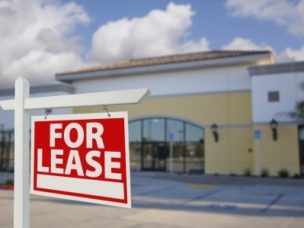 a red and white "for lease" sign in focused with a bulding in the background