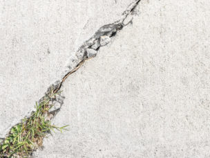 Grass and weeds growing in cracked sidewalk. Close up, top down view.