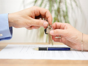 hand passing a set of keys over to another hand over a small pile of papers