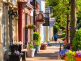 Colorful row of quaint shops and businesses with woman walking dog on the sidewalk.