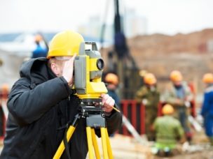 a man with yellow construction hat looking through a Surveyor theodolite on tripod